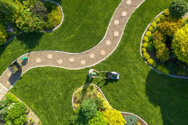 Aerial view of a large garden with a grass field being mowed by a Caucasian gardener during summer.